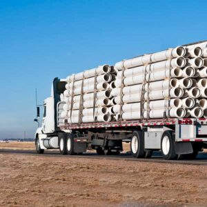 Flatbed truck transporting large white PVC pipes on a highway