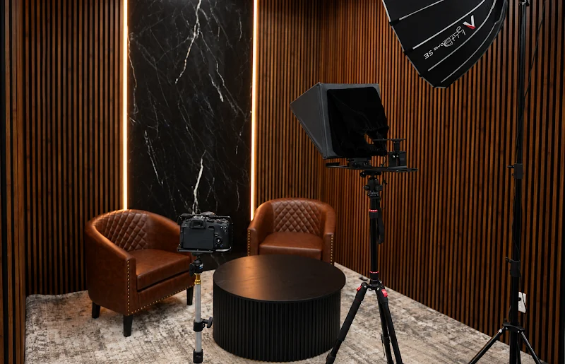 Wood-panel podcast studio with leather chairs, softbox lighting and teleprompter camera rig